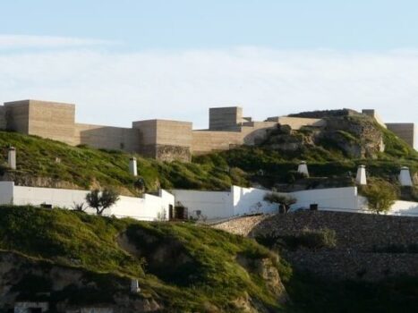 Stone fortress walls on a grassy hillside beneath a bright blue sky